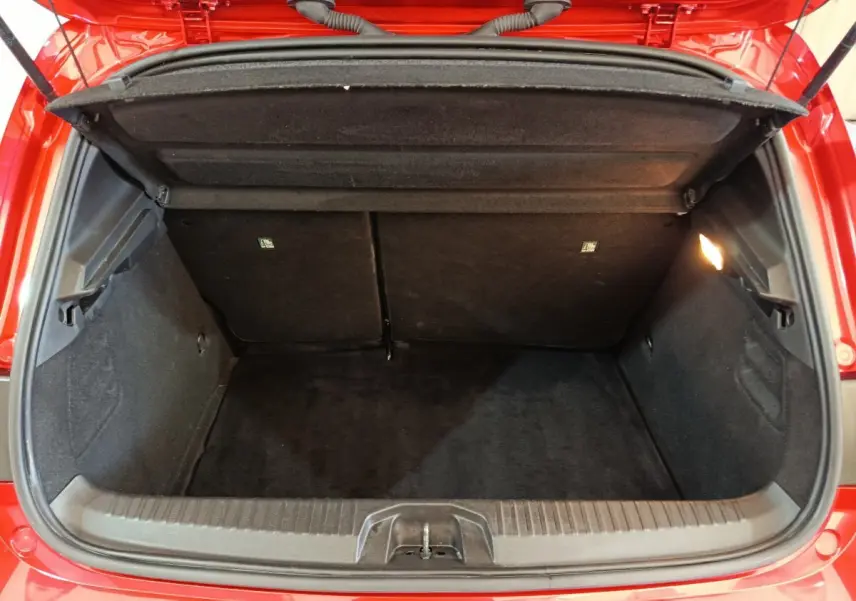 Coffre ouvert vu de l'arrière d'une Renault Clio Techno TCe 90 rouge, montrant un espace de chargement propre et éclairé.