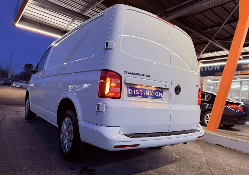 Vue 3/4 arrière droite d’un Volkswagen Transporter blanc L1H1 avec feux allumés et plaque Distinxion.