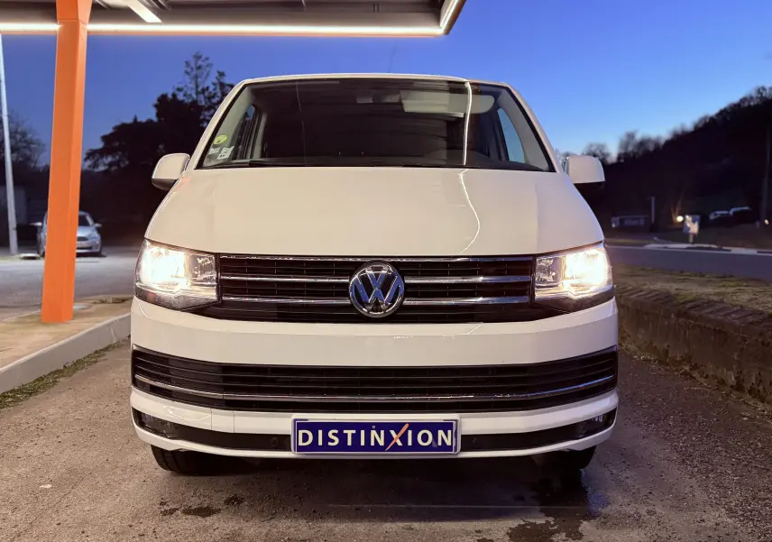 Vue avant d’un Volkswagen Transporter L1H1 blanc de 2018 avec phares allumés et plaque Distinxion visible.
