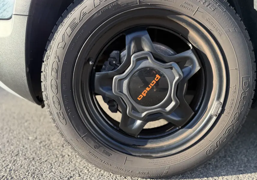 Gros plan sur la roue avant droite de la Fiat Panda City Cross gris minuit avec jante noire et logo orange Panda.