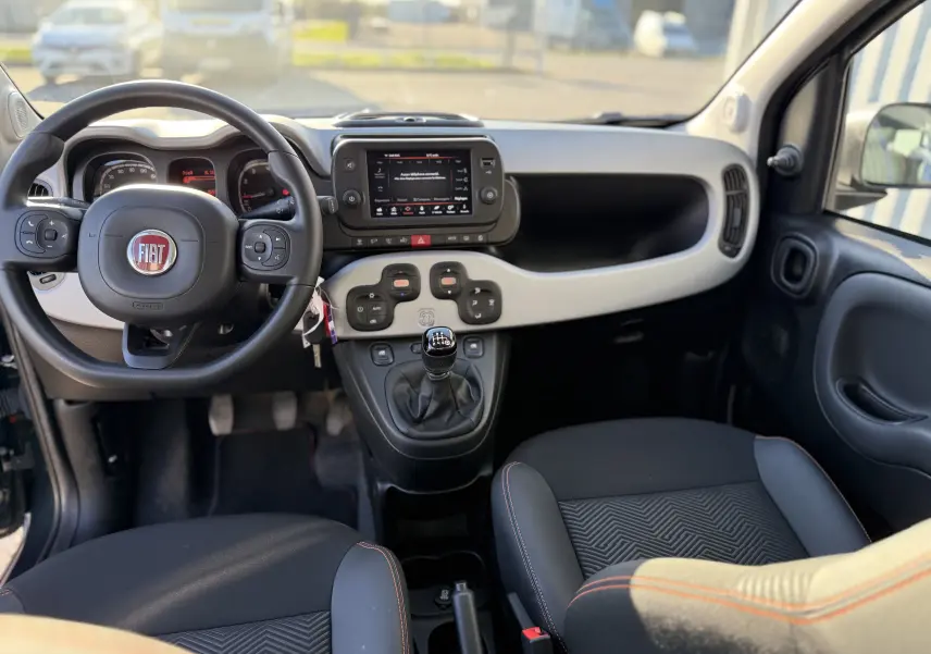 Vue intérieure avant de la Fiat Panda City Cross 2023, tableau de bord gris clair avec volant noir et levier de vitesses manuel.