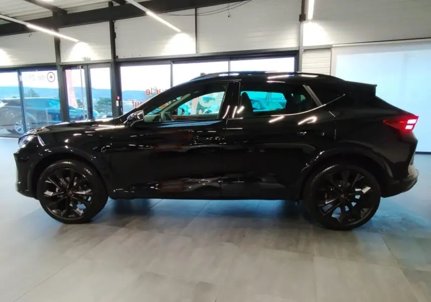 Profil droit du CUPRA Formentor noir métal avec jantes noires et feux arrière allumés en intérieur showroom.