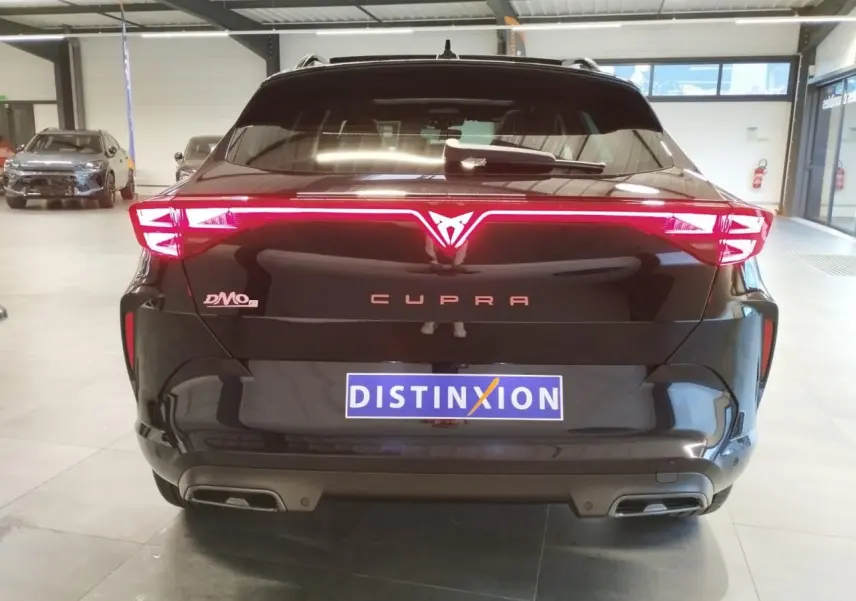 Vue arrière d'une CUPRA Formentor noire métallisée avec feux arrière Tri-LED allumés en intérieur showroom.