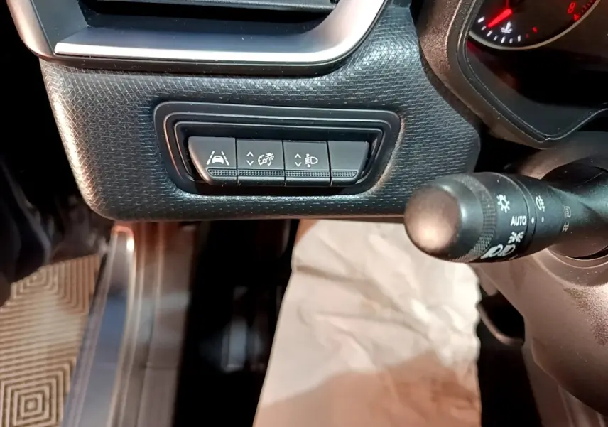 Gros plan sur les commandes d'assistance à la conduite sous le tableau de bord d'une Renault Clio gris foncé, côté gauche.