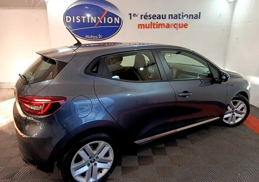 Renault Clio Business TCe 90 gris foncé vue de profil droit en intérieur avec jantes alliage et feux arrière allumés.