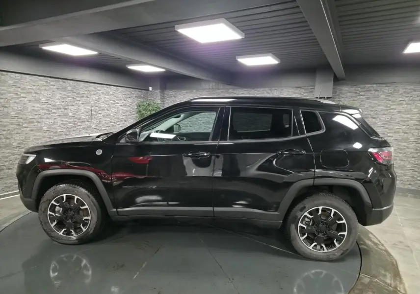 Jeep Compass Trailhawk noir en profil côté gauche, avec jantes alliage 17'' et vitres surteintées dans un garage.