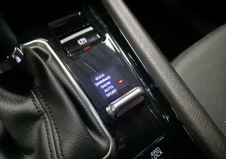 Gros plan sur la console centrale noire du Jeep Compass 2024, montrant la sélection des modes tout-terrain et frein de stationnement électrique.