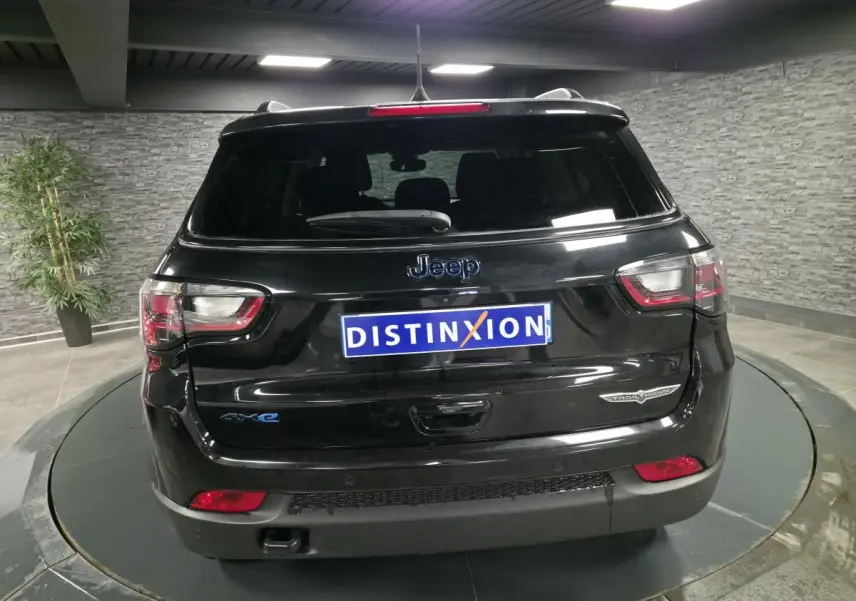 Vue arrière d'un Jeep Compass Trailhawk noir brillant avec badges Trailhawk et 4xe en intérieur showroom.