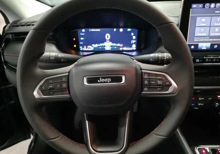 Vue rapprochée du volant cuir noir avec surpiqûres rouges et tableau de bord numérique du Jeep Compass Trailhawk 2024.
