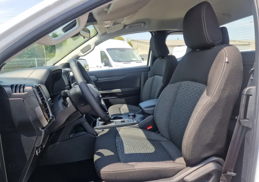 Vue intérieure côté conducteur du Ford Ranger Super Cabine blanc, sièges tissu noir avec motifs et console centrale visible.