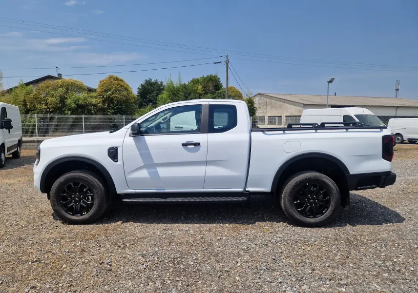 Ford Ranger Super Cabine blanc vu de profil côté gauche, avec jantes noires et plateau équipé de barres et rideau rigide.