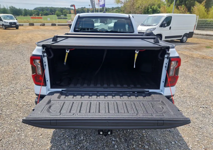 Vue arrière d’un Ford Ranger Super Cabine blanc avec plateau ouvert et rideau rigide coulissant partiellement relevé.
