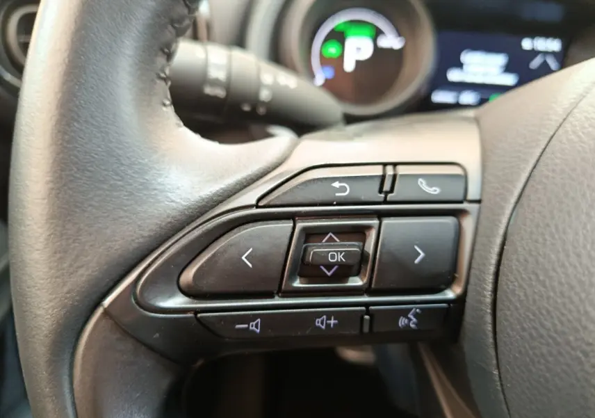 Gros plan sur les commandes multifonctions noires du volant cuir de la Toyota Yaris Hybride 116h 2023.