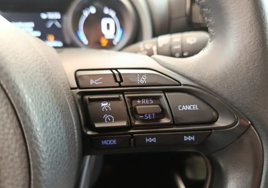 Gros plan sur les commandes du volant cuir à droite de la Toyota Yaris hybride gris clair 2023, affichage digital en arrière-plan.