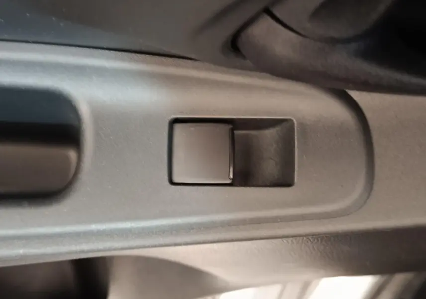 Gros plan sur le bouton de commande de la vitre côté conducteur dans l'habitacle gris foncé d'une Toyota Yaris Hybride 2023.
