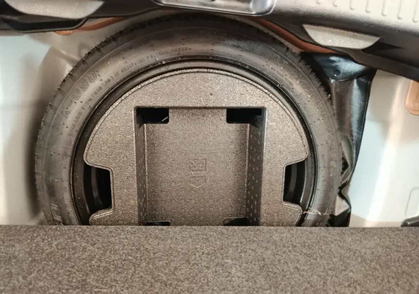 Gros plan sur la roue de secours dans le coffre d'une Toyota Yaris hybride gris clair, vue de dessus.
