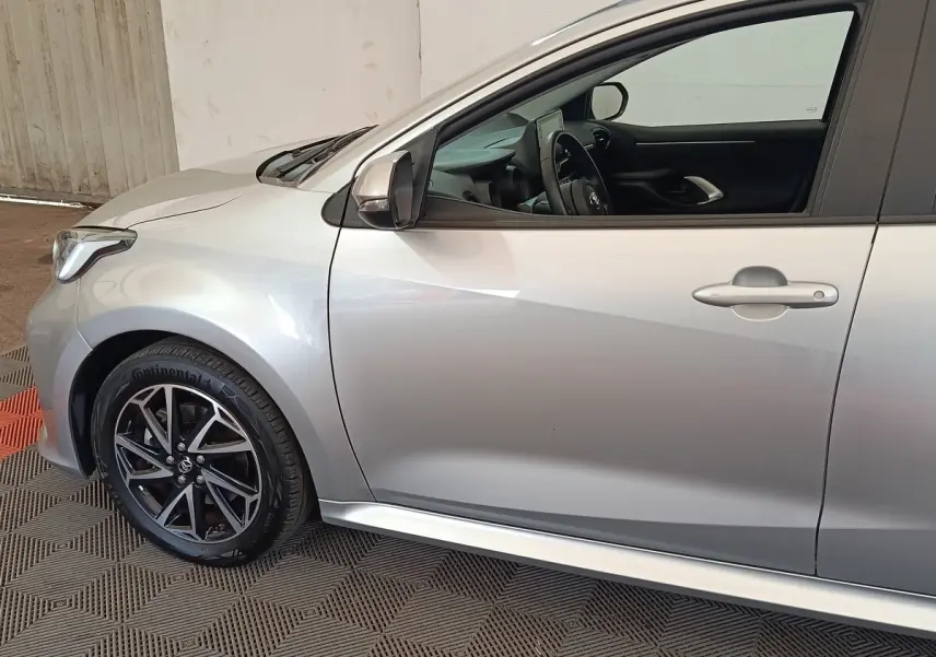 Vue latérale côté gauche d'une Toyota Yaris hybride gris clair avec jante alliage noir et intérieur visible.