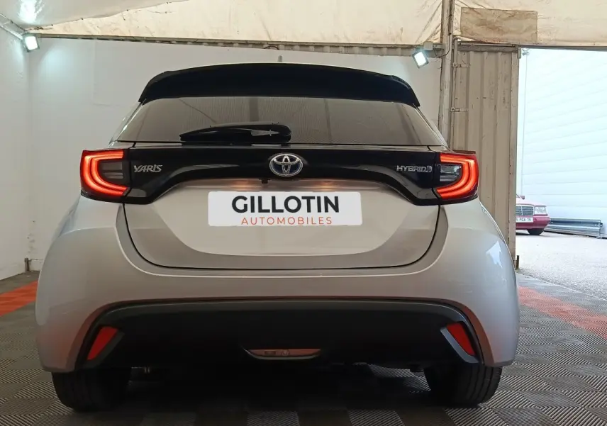 Vue arrière d'une Toyota Yaris hybride gris clair avec feux arrière LED en forme de C et bande noire distinctive.