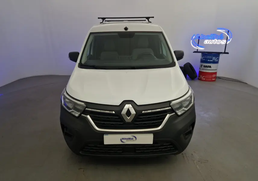 Vue avant d'un Renault Kangoo blanc 2023 avec calandre noire et barre de toit dans un studio lumineux.