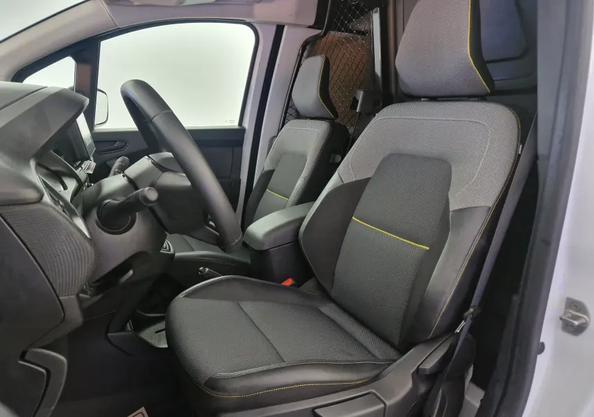 Vue intérieure côté conducteur du Renault Kangoo blanc 2023, sièges tissu gris avec surpiqûres jaunes et grille de séparation métallique.