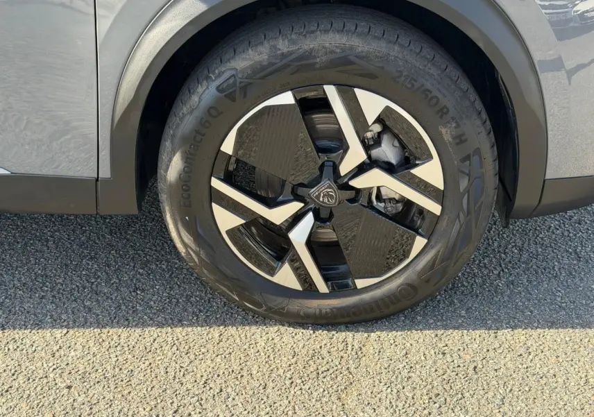 Gros plan sur la roue avant droite en jante alu bicolore du Peugeot e-2008 gris Artense, avec partie de la carrosserie visible.