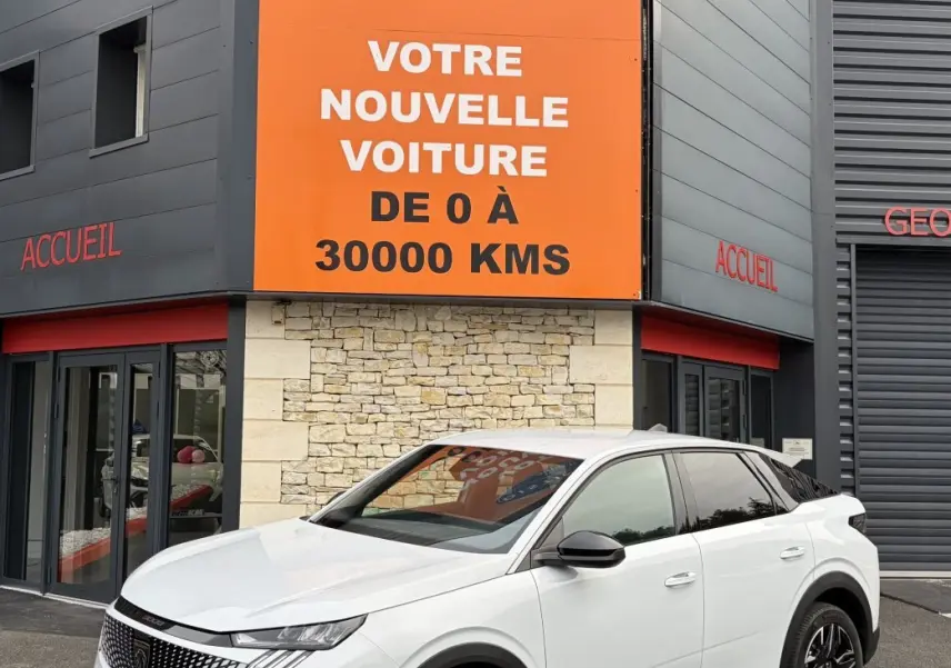 Peugeot 3008 blanc en 3/4 avant droit, avec jantes noires et calandre distinctive, devant un bâtiment commercial.