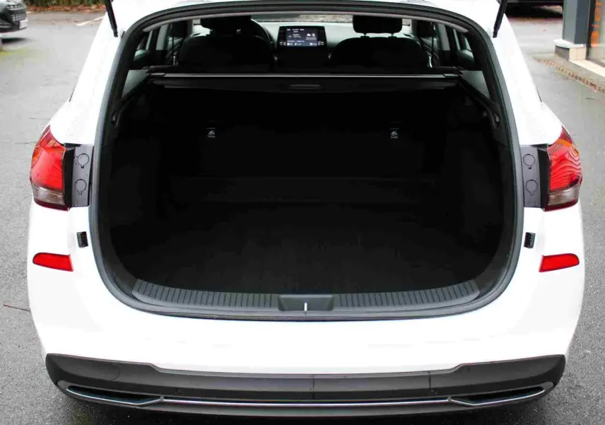 Vue arrière ouverte du coffre d'une Hyundai i30 SW blanche polaire, montrant l'espace de chargement et l'intérieur sombre.