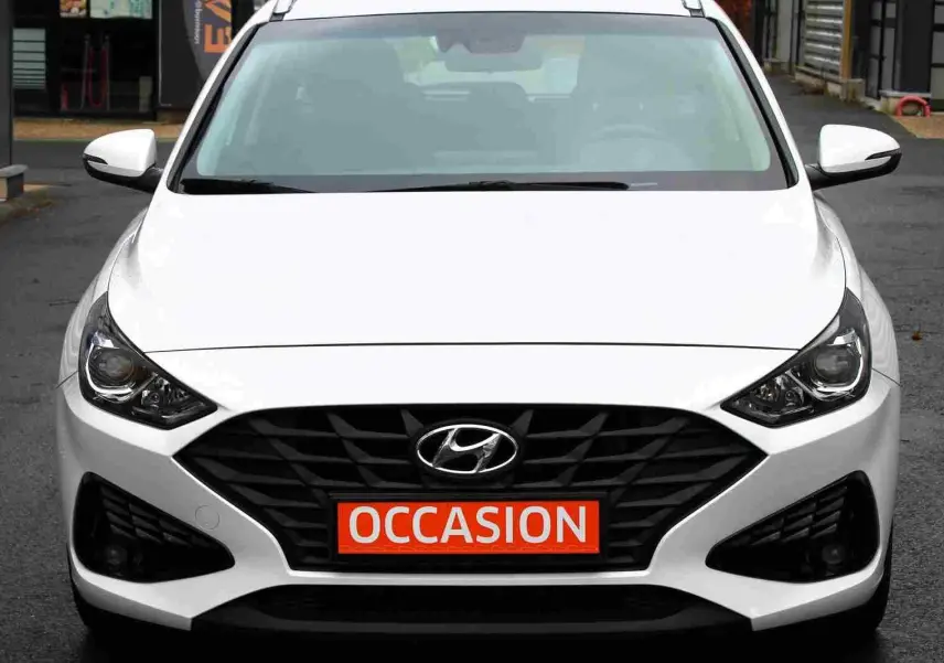 Vue frontale d'une Hyundai i30 SW blanche polaire avec calandre noire et plaque "OCCASION" rouge visible.