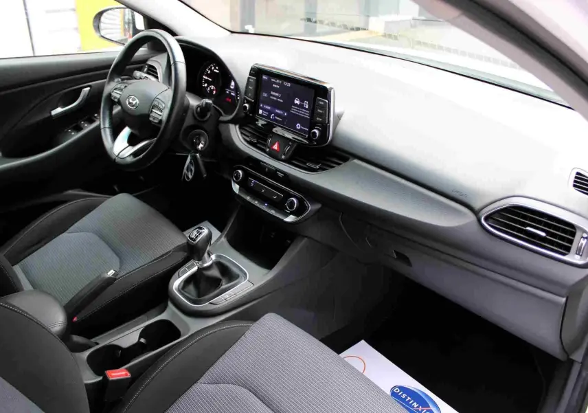 Vue intérieure côté conducteur de la Hyundai i30 SW 2022, avec tableau de bord moderne et sellerie tissu gris noir.