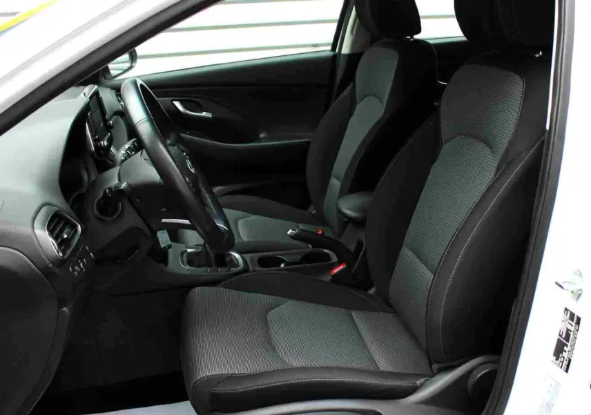 Intérieur côté conducteur d'une Hyundai i30 SW blanc polaire 2022, sièges tissu gris et noir, volant et tableau de bord visibles.