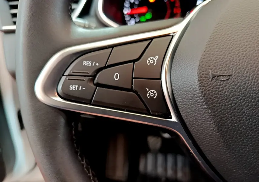 Gros plan sur les commandes de régulateur de vitesse au volant cuir noir de la Renault Clio Business TCe 100 blanche.