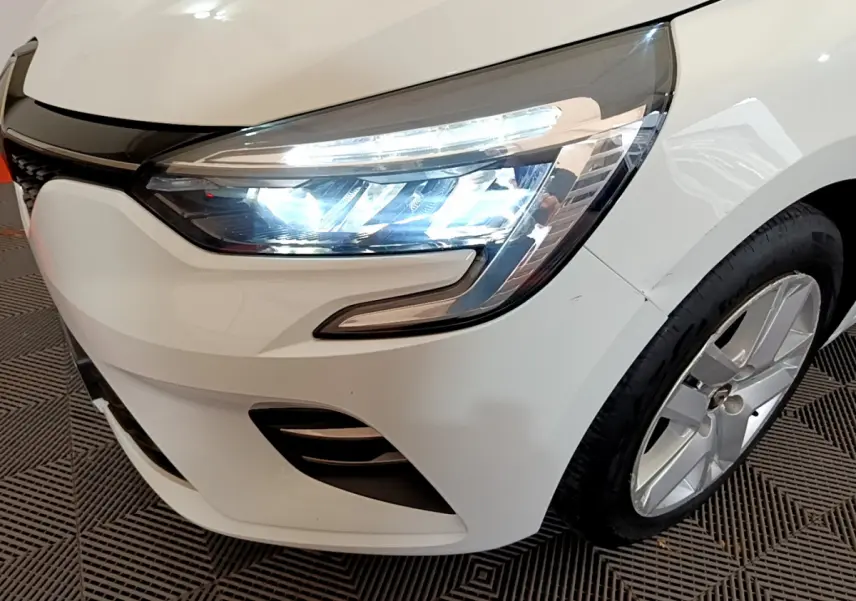 Gros plan sur l'avant droit d'une Renault Clio Business TCe 100 blanche, mettant en valeur le phare LED et la jante alliage.