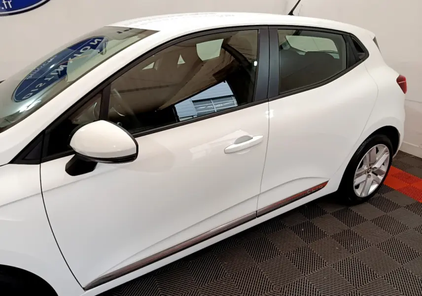 Profil côté gauche d'une Renault Clio Business blanche, avec rétroviseur assorti et jantes alliage visibles.