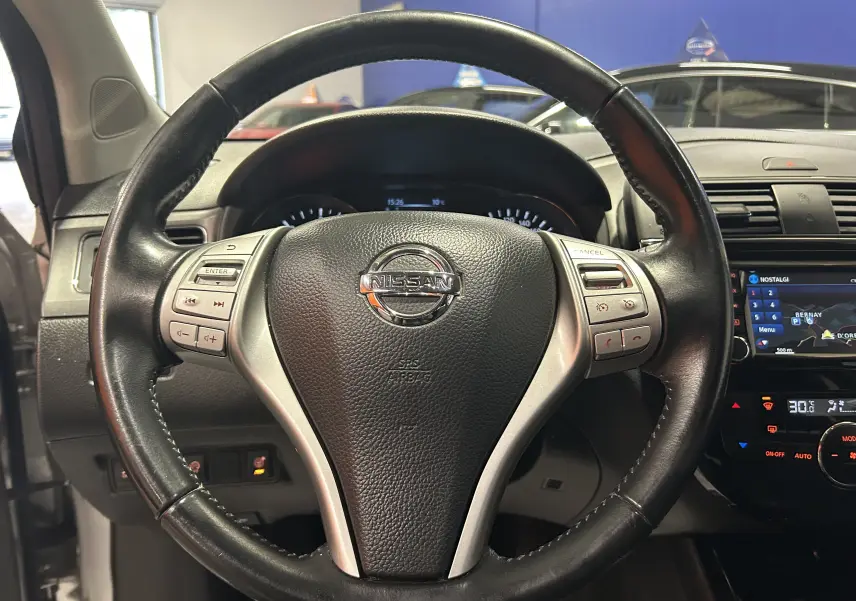 Vue centrée sur le volant cuir noir de la Nissan Pulsar 2018 avec tableau de bord et écran GPS visible à droite.