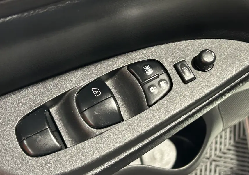 Gros plan sur les commandes de lève-vitres et réglages des rétroviseurs côté conducteur d’une Nissan Pulsar gris 2018.