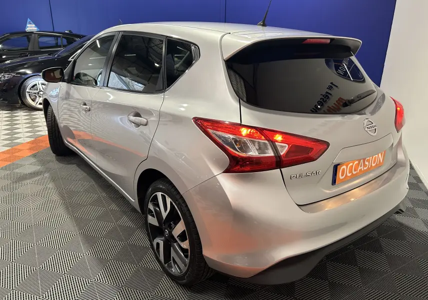 Vue 3/4 arrière droite d'une Nissan Pulsar gris métallisé avec feux arrière allumés dans un showroom.