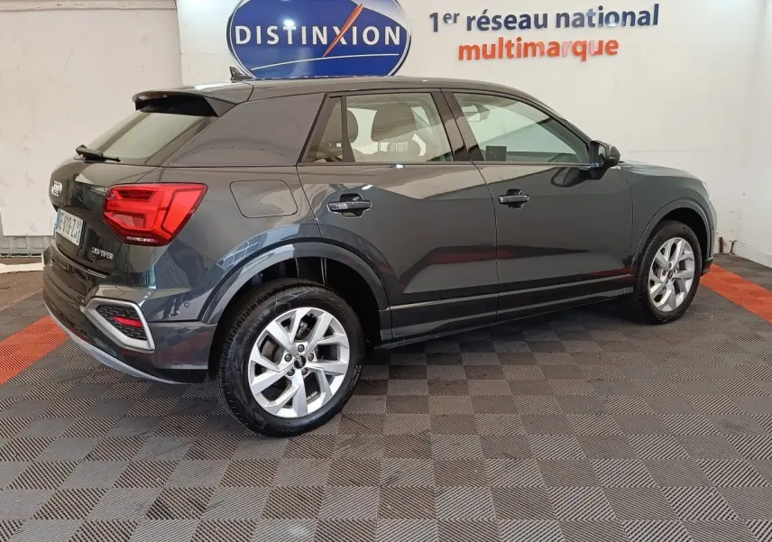 Audi Q2 gris foncé vue de profil côté droit, avec jantes alliage et feux arrière LED visibles en intérieur showroom.