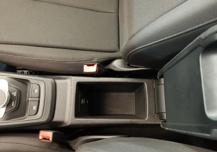 Vue plongeante sur la console centrale noire de l'Audi Q2 35 TFSI 150 S Tronic Business Line avec accoudoir et sièges gris foncé.