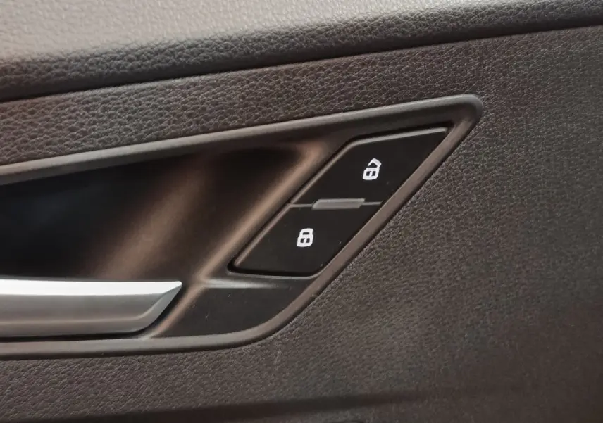 Détail de la commande de verrouillage des portes sur la porte intérieure noire d’un Audi Q2 gris foncé.