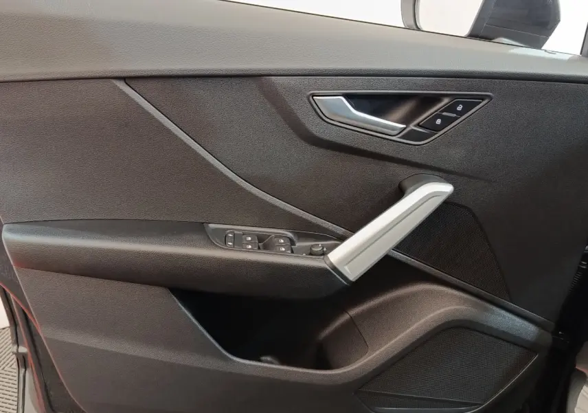 Détail de la porte côté conducteur d’un Audi Q2 gris foncé 2022, avec poignée argentée et commandes électriques.