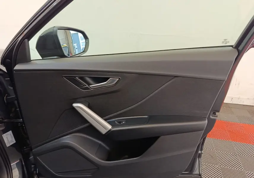 Vue côté intérieur de la porte avant gauche de l'Audi Q2 gris foncé, avec poignée argentée et miroir extérieur visible.