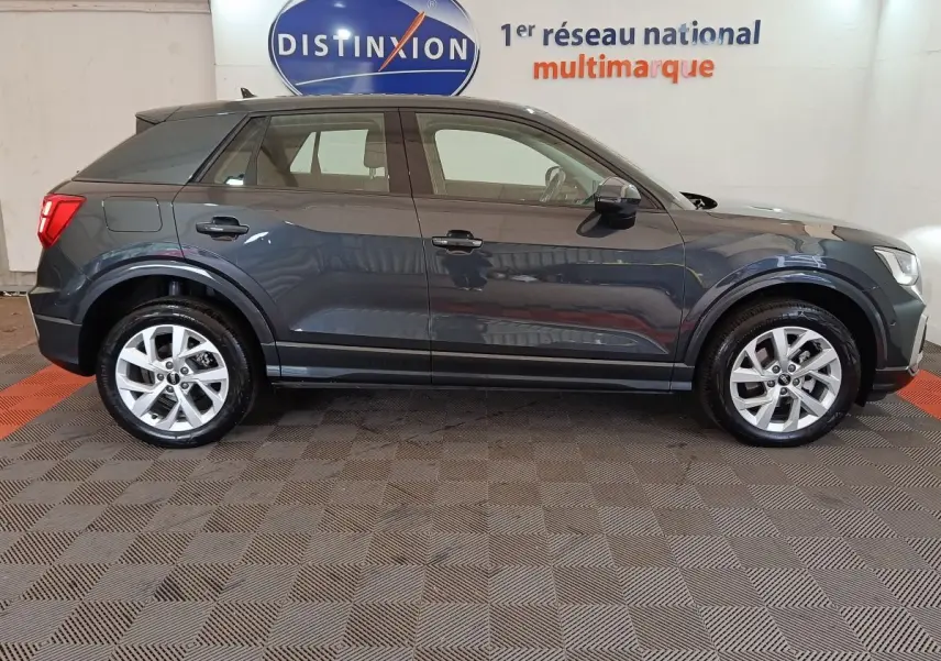 Profil côté gauche d'un Audi Q2 gris foncé 2022, version Business Line, sur sol intérieur avec logo Distinxion en arrière-plan.