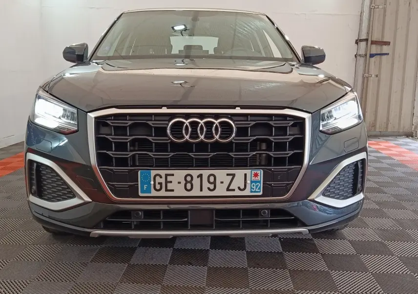 Vue frontale d'un Audi Q2 gris foncé 2022 avec calandre noire et phares LED allumés dans un garage.