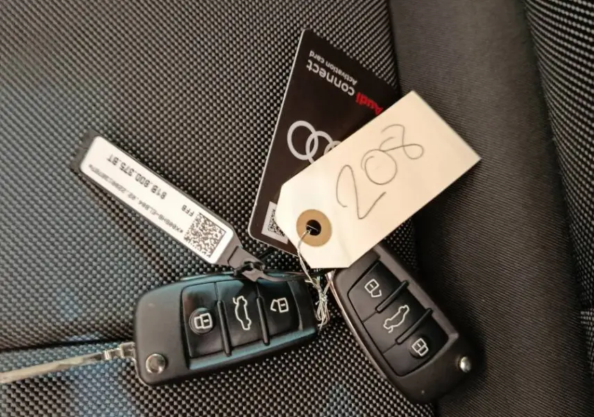 Gros plan sur deux clés Audi noires posées sur un siège tissu gris foncé à motifs fins.