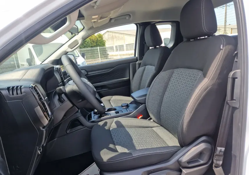 Vue intérieure côté conducteur du Ford Ranger Super Cabine blanc, montrant les sièges avant et le tableau de bord moderne.