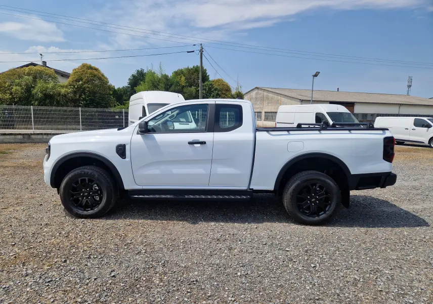 Vue latérale droite du Ford Ranger Super Cabine blanc avec roues noires et plateau équipé de barres et rideau rigide.