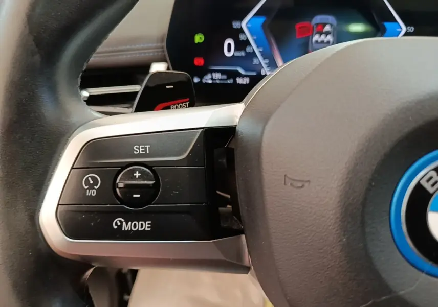 Gros plan sur le volant alu et cuir gris foncé du BMW X1 xDrive25e M Sport avec commandes multifonctions et affichage digital en arrière-plan.