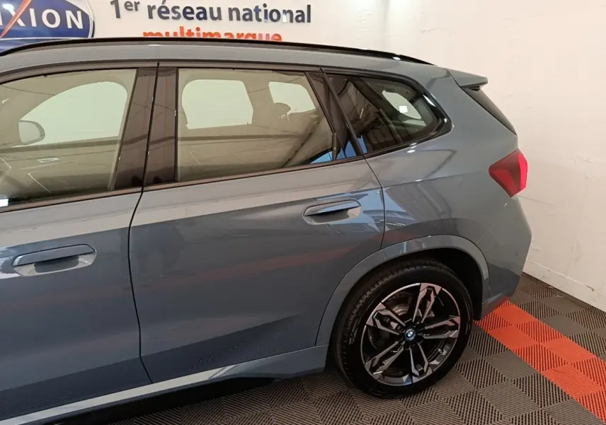 Vue latérale droite d’un BMW X1 xDrive25e M Sport gris foncé avec jantes noires et toit noir dans un showroom.