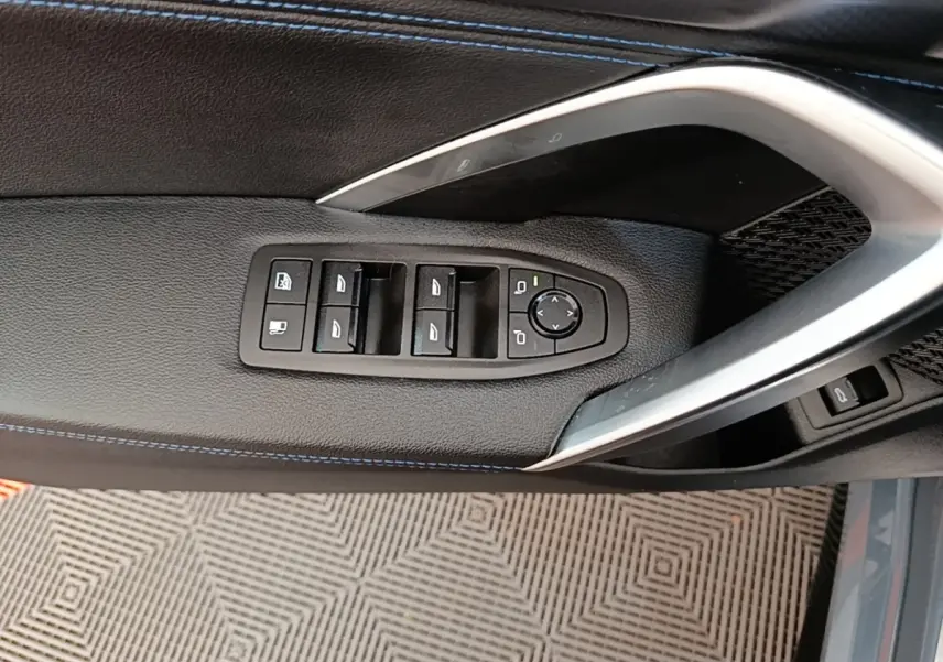 Vue rapprochée de la porte côté conducteur du BMW X1 gris foncé, avec commandes des vitres et rétroviseurs intégrées.