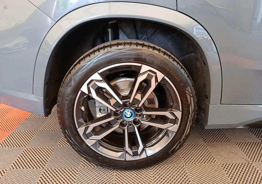 Gros plan sur la roue avant droite d’un BMW X1 gris foncé avec jante alliage au design géométrique.